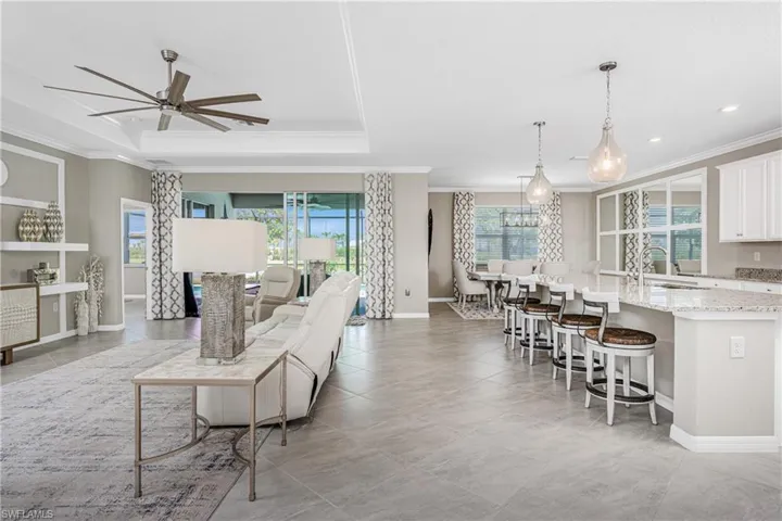Living area with crown molding, a raised ceiling, a ceiling fan, and recessed lighting