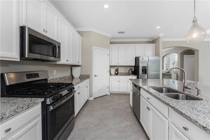 Kitchen with crown molding, white cabinetry, arched walkways, a sink, and appliances with stainless steel finishes