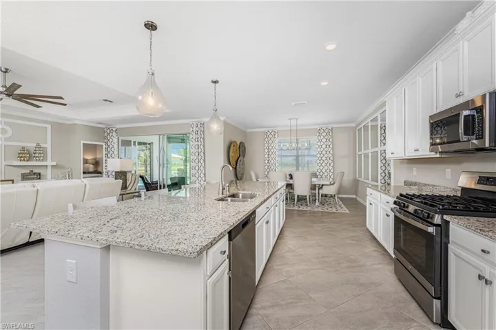 Kitchen with crown molding, appliances with stainless steel finishes, a sink, white cabinets, and an island with sink