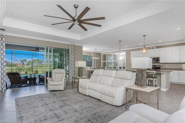 Living room featuring crown molding, plenty of natural light, light tile patterned floors, and ceiling fan with notable chandelier