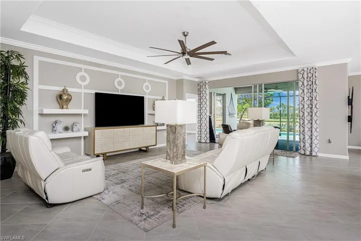 Tiled living area featuring ceiling fan, ornamental molding, and a tray ceiling