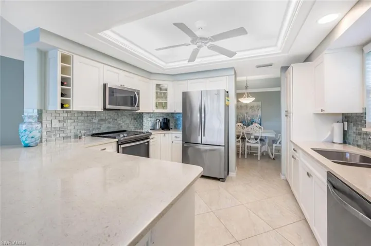 Kitchen featuring decorative backsplash, a raised ceiling, appliances with stainless steel finishes, white cabinetry, and light stone counters