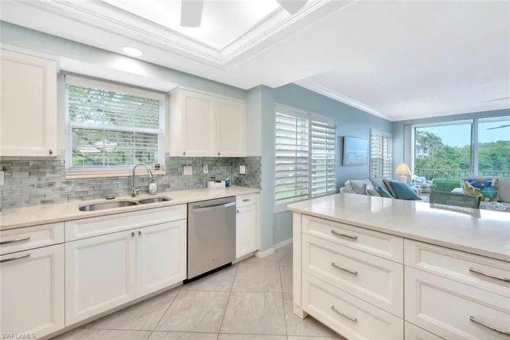 Kitchen with light stone countertops, white cabinets, ornamental molding, open floor plan, and dishwasher