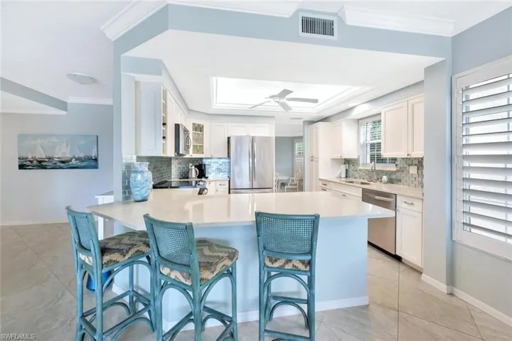 Kitchen featuring crown molding, appliances with stainless steel finishes, a kitchen breakfast bar, tasteful backsplash, and white cabinets