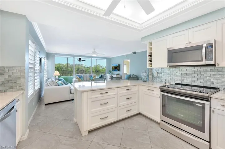 Kitchen featuring backsplash, appliances with stainless steel finishes, crown molding, open floor plan, and light stone counters