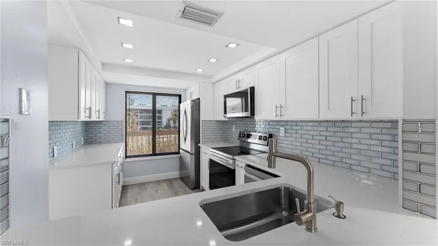 Kitchen featuring decorative backsplash, light stone countertops, appliances with stainless steel finishes, white cabinetry, and recessed lighting
