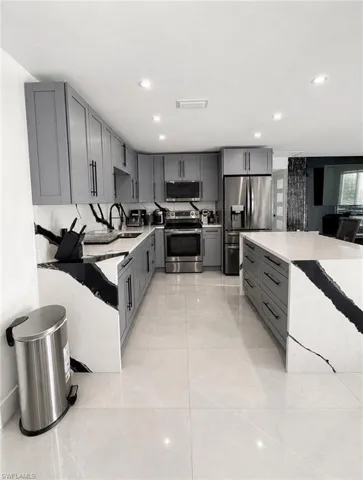 Modern kitchen featuring light gray cabinetry, stainless steel appliances, a large center island, distinctively veined countertops, and recessed lighting