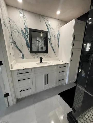White shaker-style vanity with a single basin sink, white stone-finish countertop, and black hardware