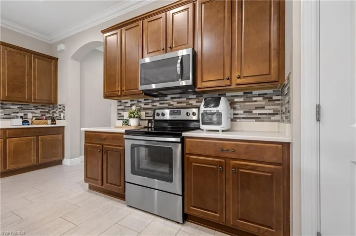 Kitchen featuring stainless steel appliances, backsplash, crown molding, brown cabinetry, and light wood-style floors