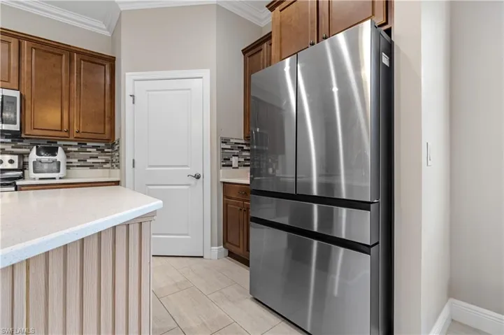Kitchen featuring stainless steel appliances, ornamental molding, light stone counters, decorative backsplash, and light tile patterned floors