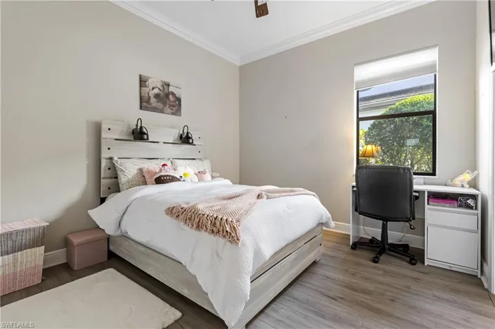 Bedroom with ornamental molding, wood finished floors, an office area, and a ceiling fan