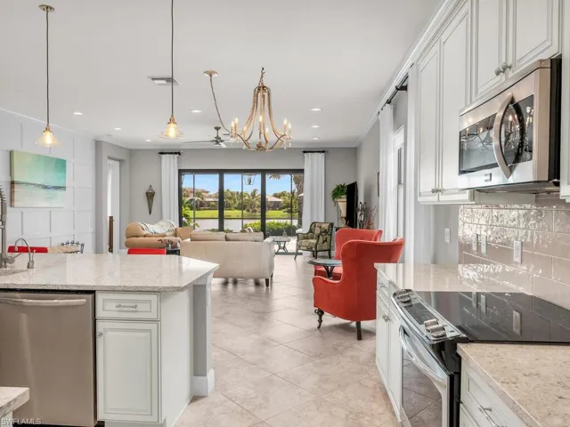 Kitchen with appliances with stainless steel finishes, white cabinets, light stone counters, backsplash, and decorative light fixtures