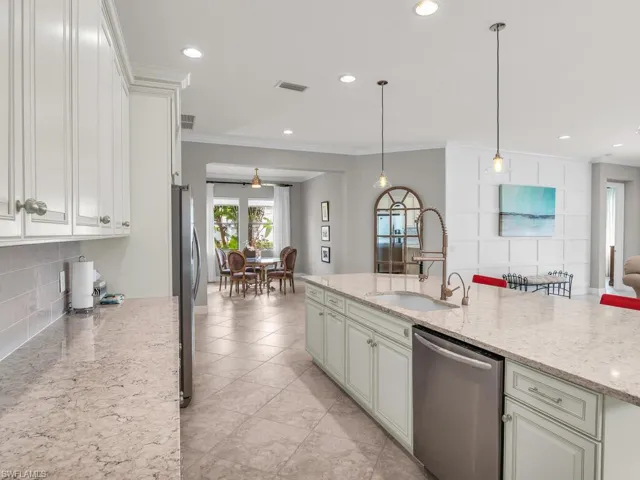 Kitchen with stainless steel appliances, sink, light stone counters, hanging light fixtures, and light tile patterned flooring