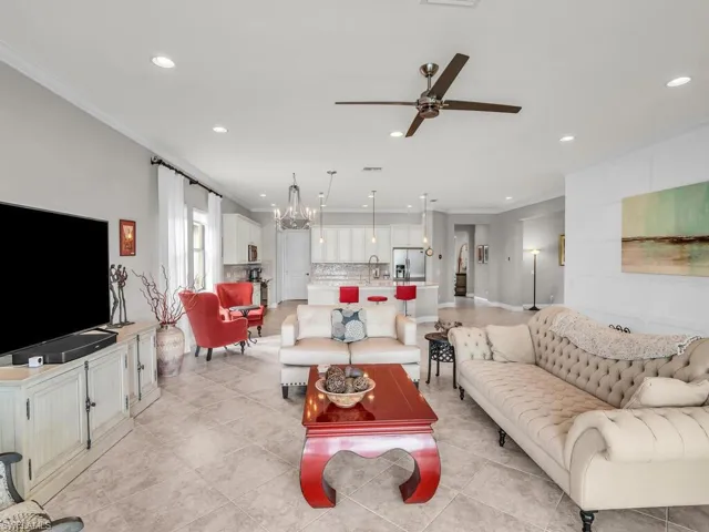 Living room with ceiling fan with notable chandelier, crown molding, sink, and light tile patterned floors