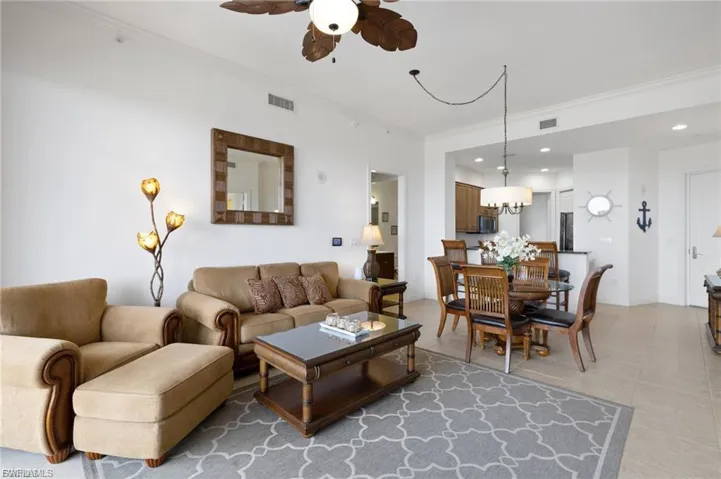 Living room featuring a ceiling fan, ornamental molding, light tile patterned flooring, and a chandelier