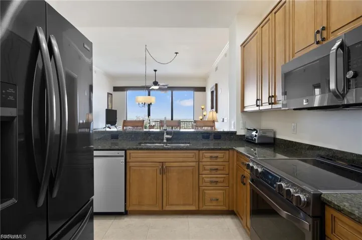 Kitchen featuring black appliances, wood finish cabinetry, dark stone countertops, hanging light fixtures, and ornamental molding