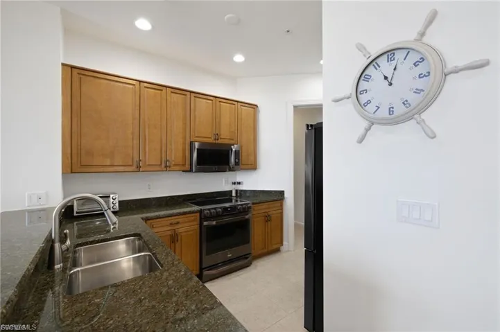 Kitchen featuring electric stove, wood finish cabinets, stainless steel microwave, dark stone countertops, and freestanding refrigerator