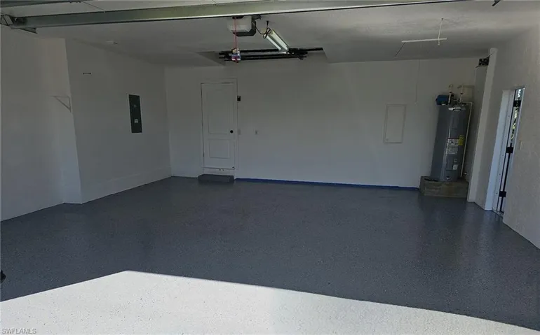Garage with electric panel, electric water heater, and a garage door opener