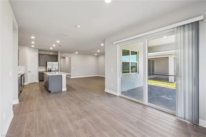 Kitchen with stainless steel fridge, light countertops, a center island with sink, light wood-style flooring, and open floor plan