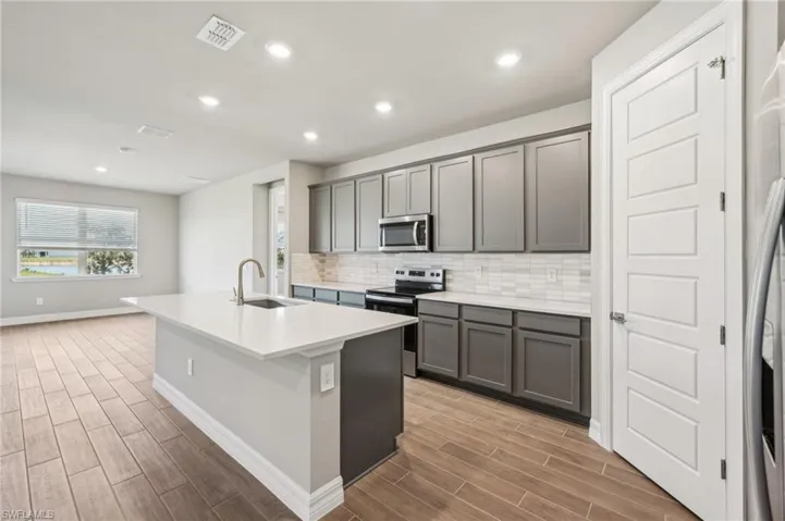 Kitchen featuring appliances with stainless steel finishes, a sink, gray cabinets, light wood finished floors, and recessed lighting