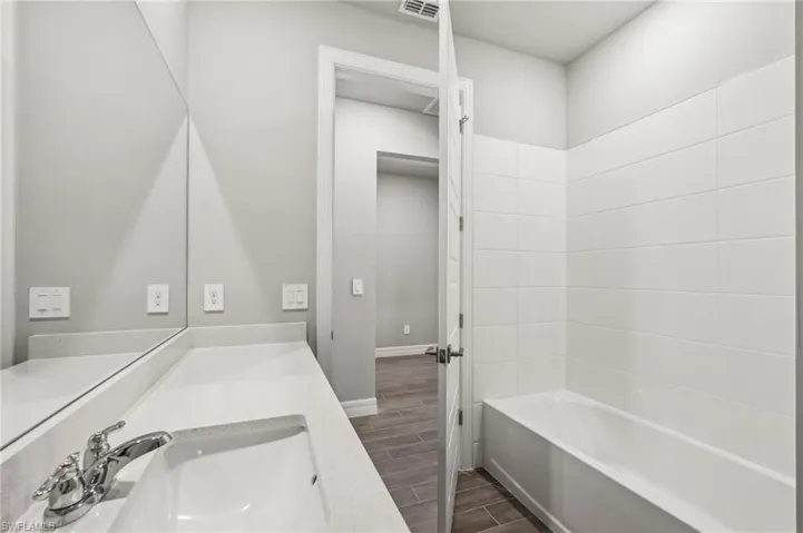 Full bath featuring wood finish floors, vanity, baseboards, and washtub / shower combination