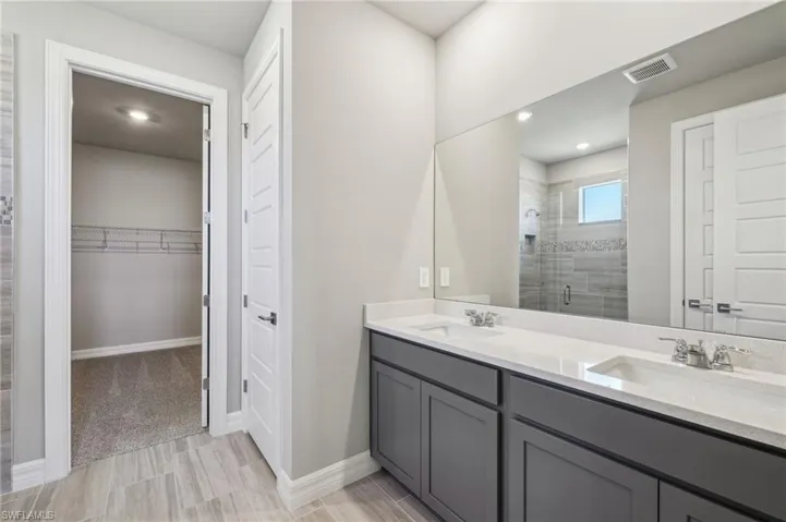 Full bath with a shower stall, a walk in closet, double vanity, baseboards, and recessed lighting