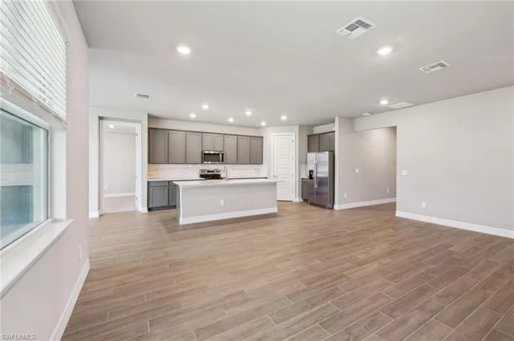 Kitchen with stainless steel appliances, open floor plan, gray cabinets, baseboards, and light countertops