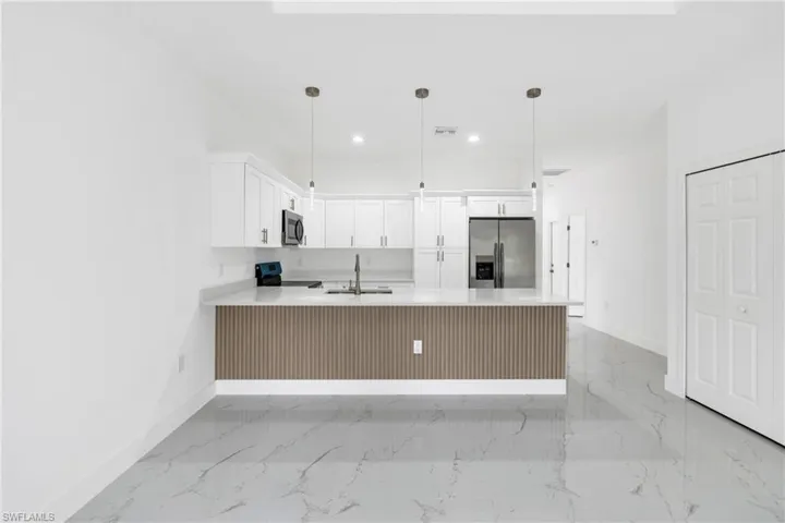 Kitchen with a peninsula, stainless steel appliances, white cabinets, pendant lighting, and light stone counters