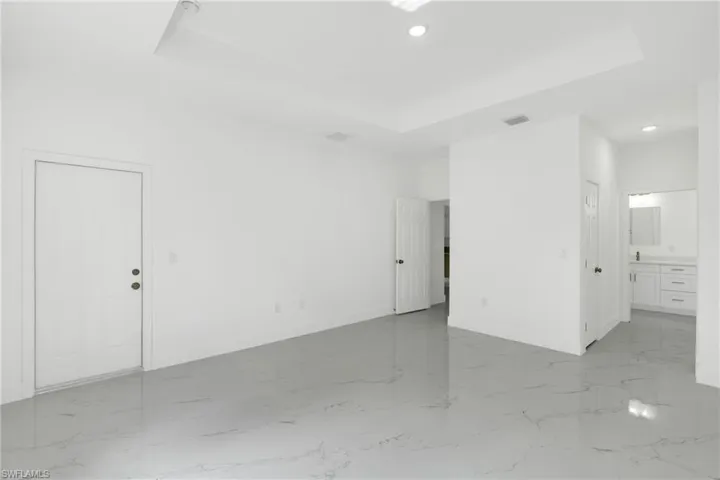 Spare room with a tray ceiling, recessed lighting, and light marble finish floors