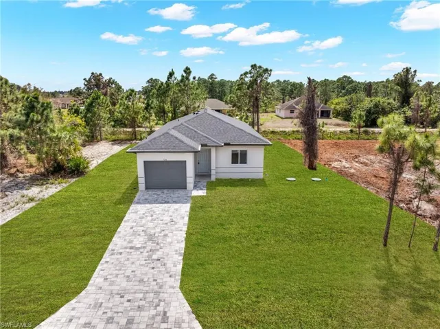 View of front facade featuring a front yard, a shingled roof, decorative driveway, an attached garage, and view of wooded area