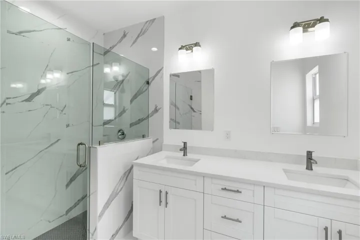 Full bath with double vanity and a marble finish shower