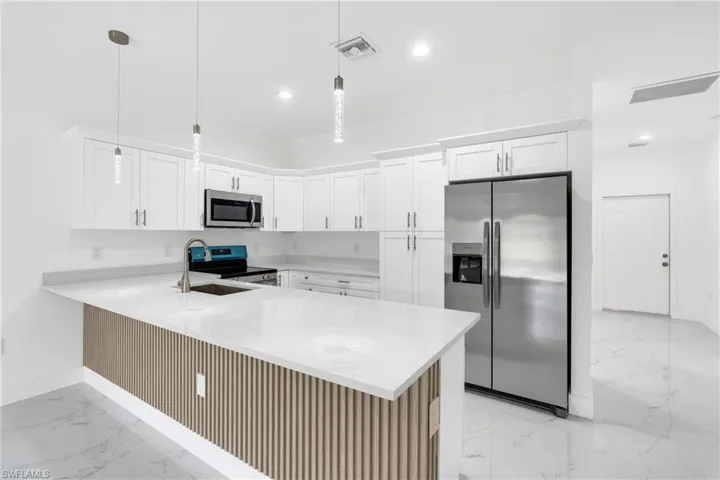 Kitchen featuring stainless steel appliances, light stone counters, a peninsula, and white cabinetry