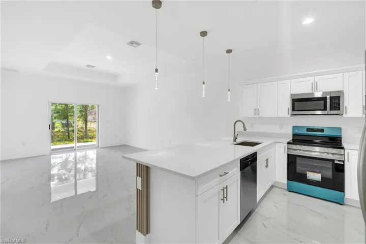 Kitchen featuring stainless steel appliances, a peninsula, light marble finish floors, white cabinetry, and a tray ceiling