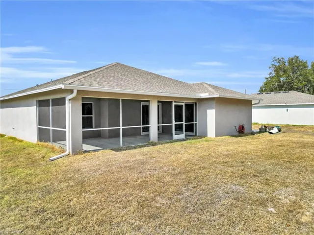 Back of house featuring a lawn, a shingled roof, stucco siding, and a sunroom