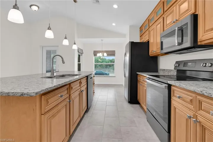 Kitchen featuring stainless steel appliances, wood finish cabinets, glass fronted cabinets, light stone counters, and lofted ceiling