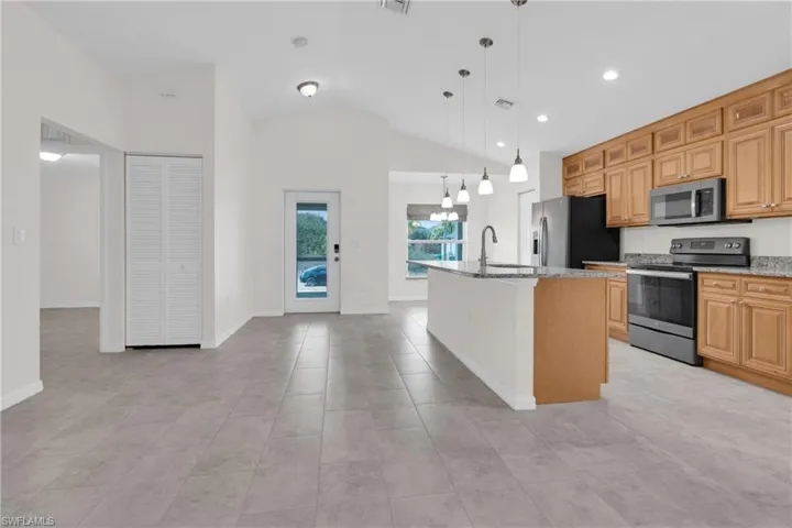 Kitchen featuring stainless steel appliances, light stone counters, pendant lighting, a kitchen island with sink, and lofted ceiling