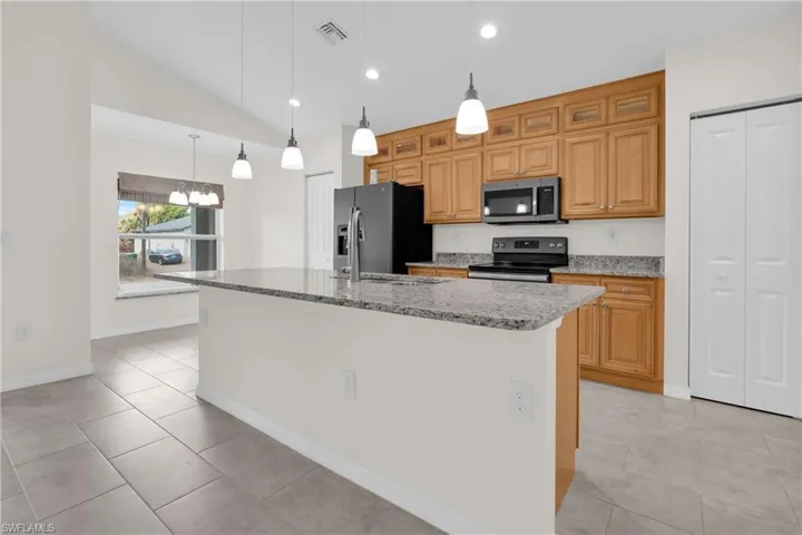 Kitchen with vaulted ceiling, light stone counters, stainless steel appliances, an island with sink, and light tile patterned floors