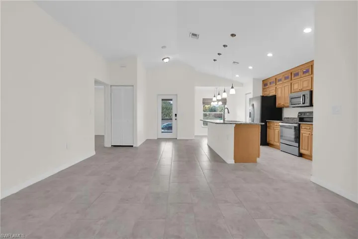 Kitchen featuring stainless steel appliances, a center island with sink, glass insert cabinets, decorative light fixtures, and open floor plan