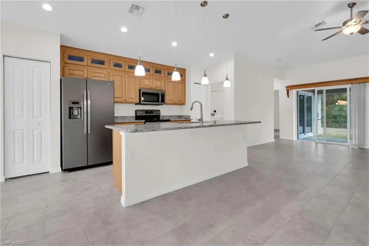Kitchen with stainless steel appliances, light stone countertops, decorative light fixtures, a center island with sink, and a ceiling fan