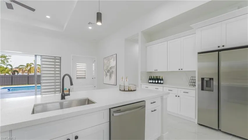 Kitchen with light stone countertops, appliances with stainless steel finishes, white cabinetry, decorative backsplash, and sink