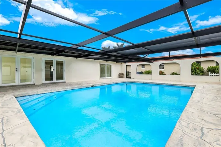 Swimming pool featuring glass enclosure, a sunroom, a patio, and french doors