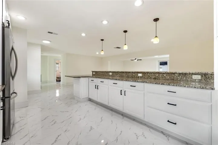 Kitchen featuring dark stone countertops, white cabinetry, recessed lighting, hanging light fixtures, and freestanding refrigerator