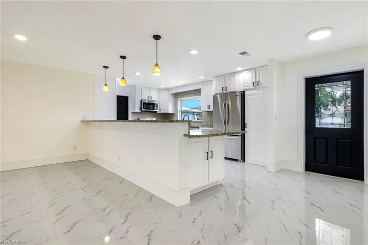 Kitchen with hanging light fixtures, dark stone countertops, white cabinets, stainless steel appliances, and a peninsula