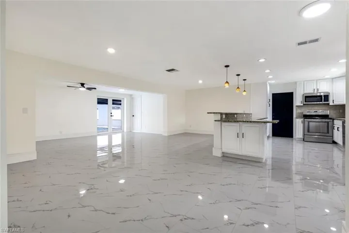 Kitchen with white cabinetry, appliances with stainless steel finishes, light marble finish flooring, hanging light fixtures, and tasteful backsplash