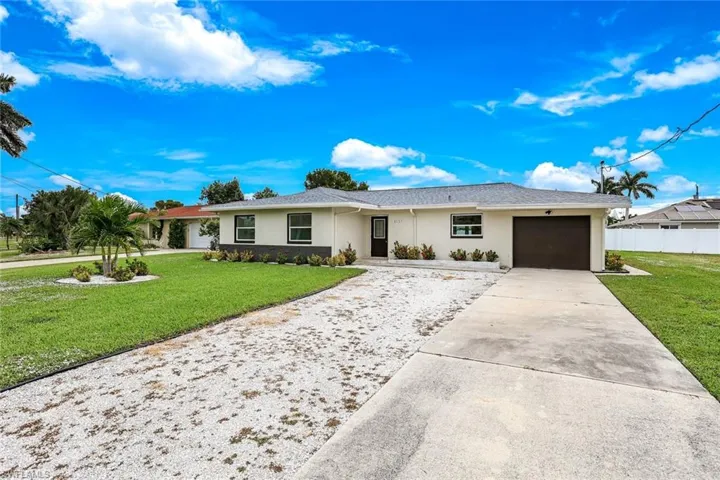 Ranch-style house featuring a front yard, stucco siding, driveway, and an attached garage