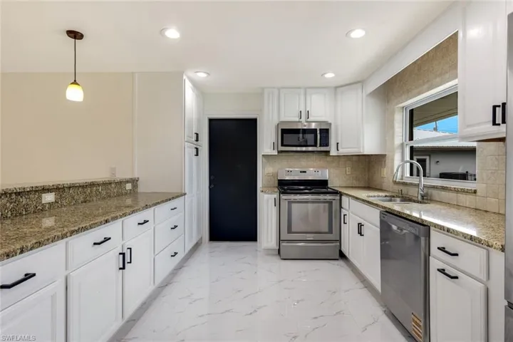 Kitchen with dark stone countertops, appliances with stainless steel finishes, pendant lighting, white cabinets, and decorative backsplash