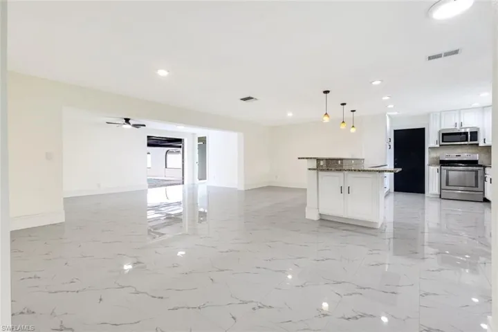 Kitchen with white cabinets, stainless steel appliances, hanging light fixtures, light marble finish floors, and dark stone countertops