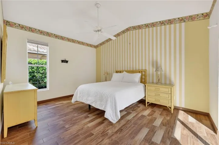 Bedroom with wood-look tile finished floors, ceiling fan, wallpapered walls, lofted ceiling, and an accent wall