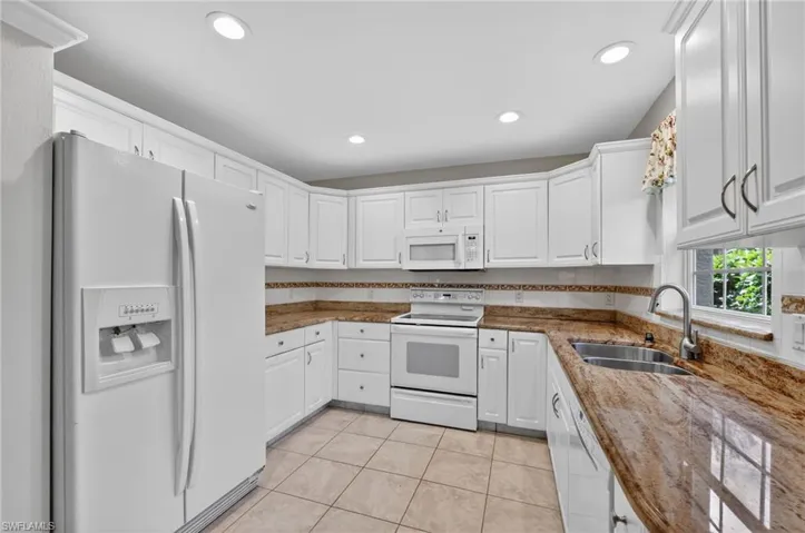 Kitchen featuring white appliances, white cabinetry, light stone counters, light tile floors, and tasteful backsplash
