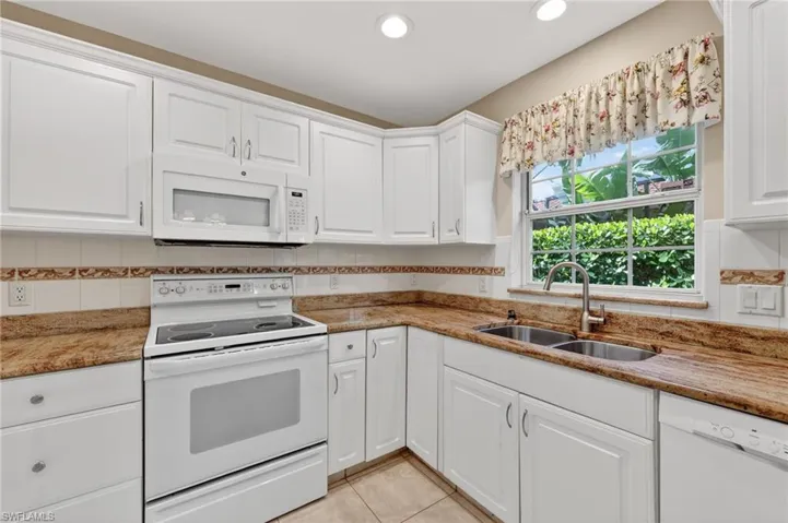 Kitchen with white appliances, backsplash, light stone countertops, and white cabinetry